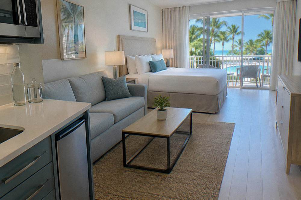 Bright hotel suite with a king bed and balcony doors opening to palms and a pool deck on Paradise Island