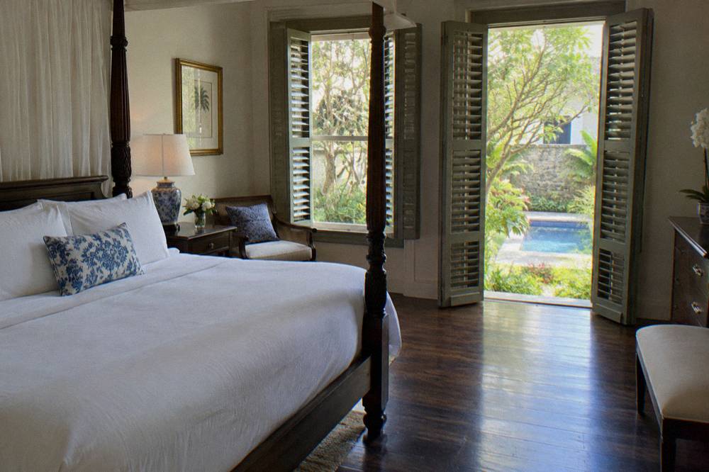 Four-poster bed with white linen in a guest room of an old Georgian mansion hotel, shutters open to a garden